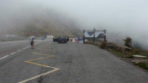 Nebliger Bergpass mit einer Straße, einem Radfahrer und einem Auto auf der Fahrbahn