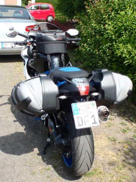 Heckansicht eines Motorrads mit Seitentaschen, geparkt neben einem Gehweg und Büschen