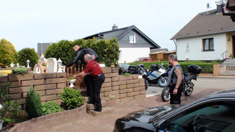 Drei Männer an Mauer in Wohnsiedlung mit Motorrädern und Auto daneben