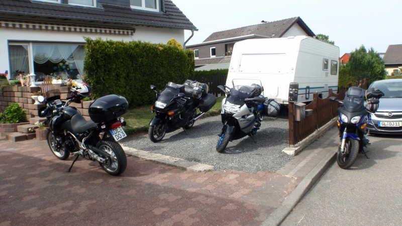 Drei Motorräder und ein Wohnwagen vor einem Haus in einem Wohngebiet