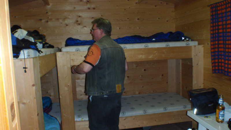 Mann steht in einem Holzraum mit Etagenbetten und einem Tisch mit Flaschen