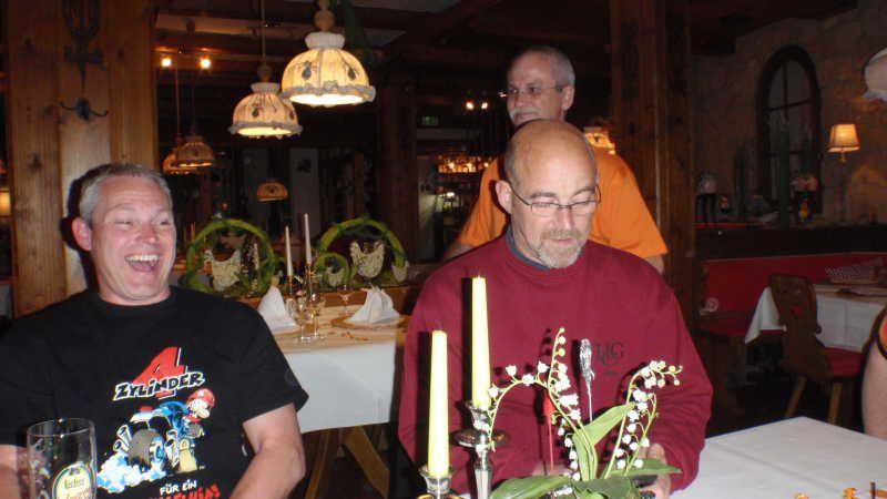 Drei Männer sitzen in einem Restaurant an einem Tisch mit Kerzen und Blumen.