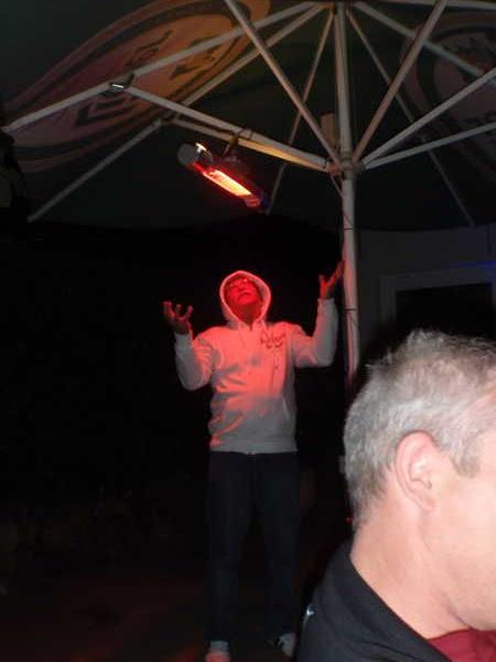 Person in weißem Hoodie steht unter einem Heizstrahler unter einem Sonnenschirm nachts