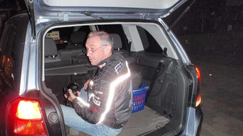Mann sitzt im geöffneten Kofferraum eines Autos bei Nacht