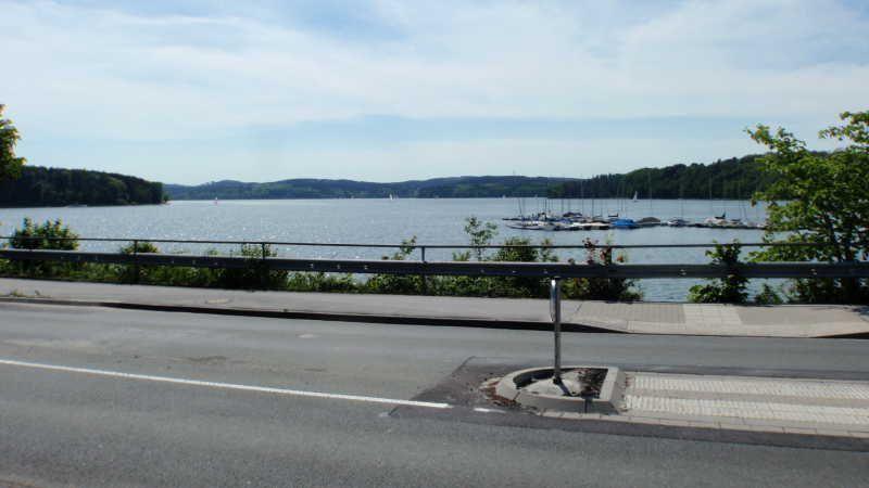 Blick auf einen See mit Segelbooten hinter einer Straße und Leitplanke