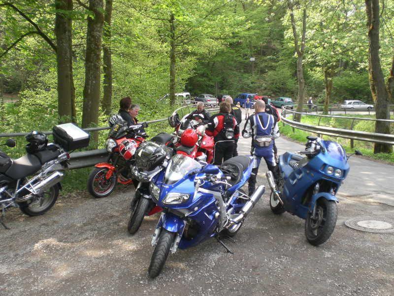 Mehrere Motorräder und Menschen in Motorradkleidung auf einem Waldweg