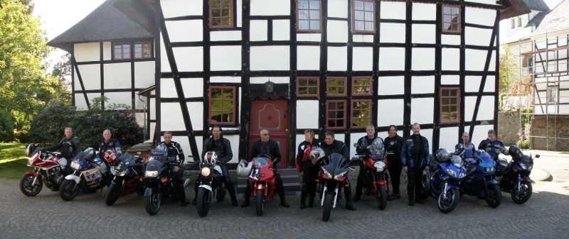 Gruppe von Motorradfahrern mit ihren Motorrädern vor einem Fachwerkhaus