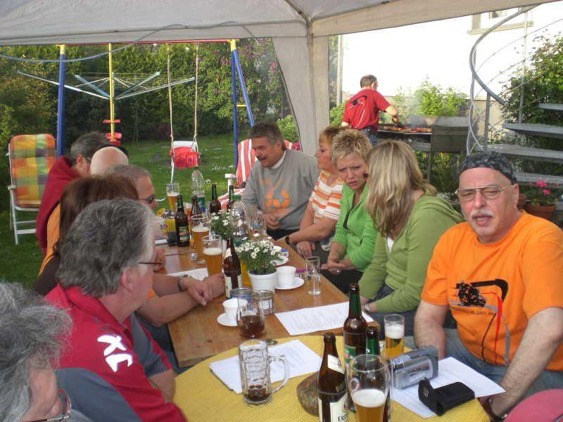 Menschen sitzen an einem Tisch im Garten unter einem Zelt mit Getränken und sprechen miteinander
