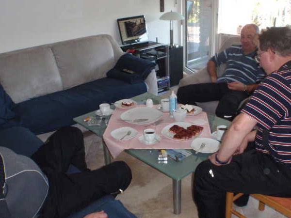 Drei Männer sitzen um einen Tisch mit Kaffee und Kuchen in einem Wohnzimmer