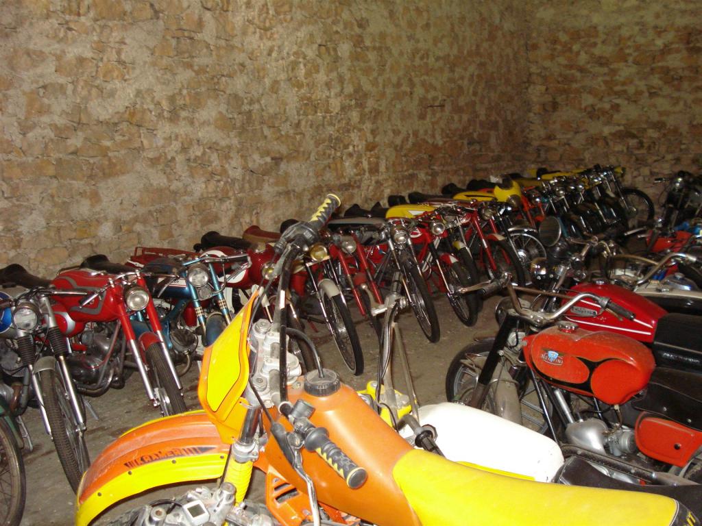 Mehrere alte und klassische Motorräder stehen in einem Raum mit Steinwand.