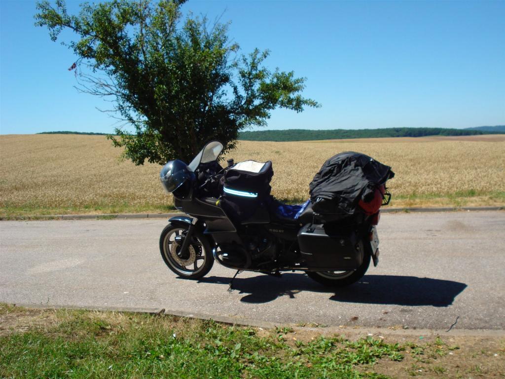 Schwarzes Motorrad mit Gepäck steht auf ruhiger Landstraße vor Feldern und klarem Himmel