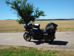 Schwarzes Motorrad mit Gepäck steht auf ruhiger Landstraße vor Feldern und klarem Himmel