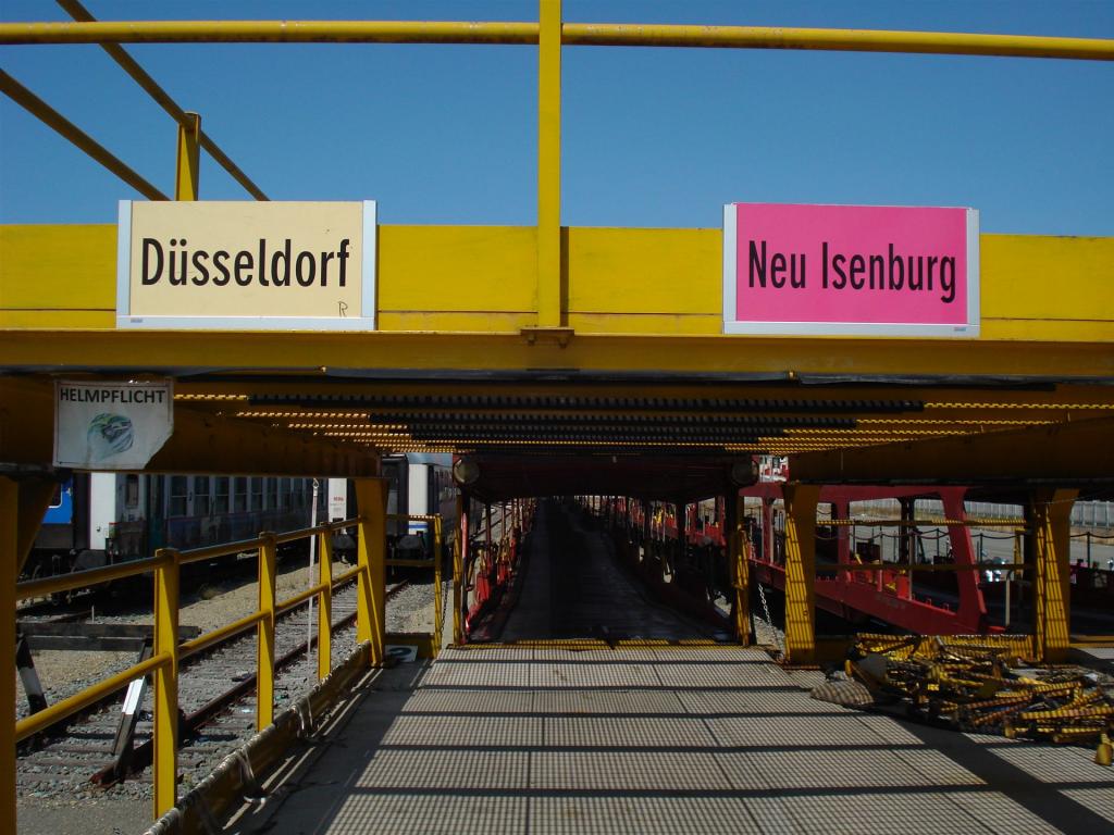 Gelbes Stahlgerüst mit zwei Wegweisschildern für Düsseldorf und Neu Isenburg über einer Bahnanlage