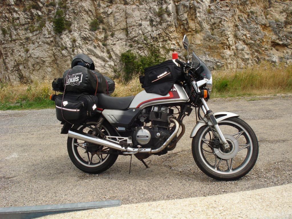 Motorrad mit Motorradhelm und Gepäcktaschen auf einer Straße vor Felswand
