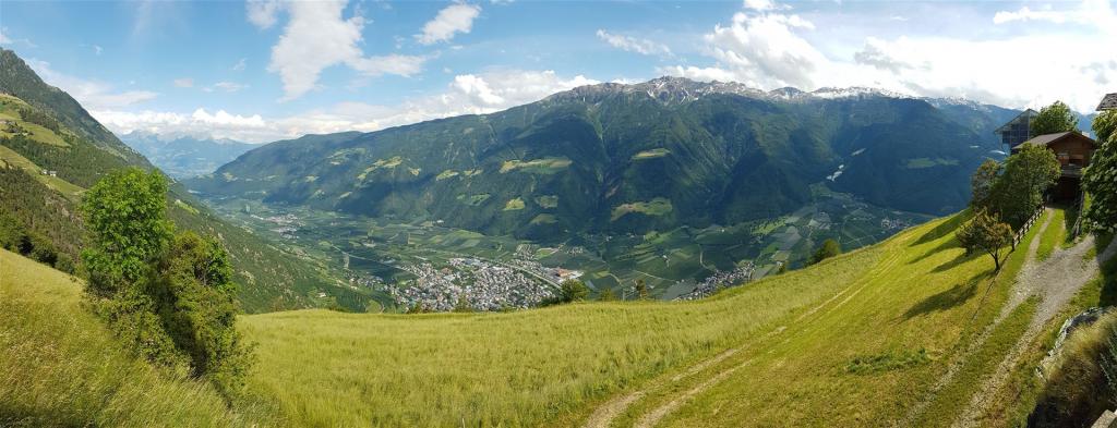 Berglandschaft mit Tal, grünen Wiesen und Häusern unter blauem Himmel