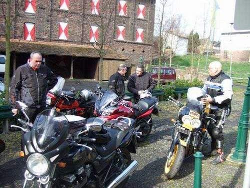 Mehrere Männer mit Motorrädern stehen vor einem Gebäude mit roten und weißen Fensterläden.