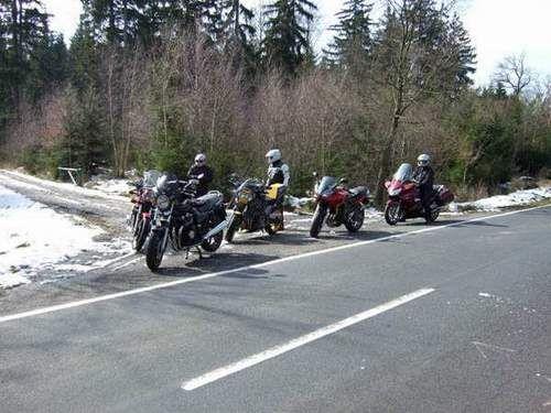 Fünf Motorräder am Straßenrand mit drei Personen in Motorradbekleidung neben einem Wald