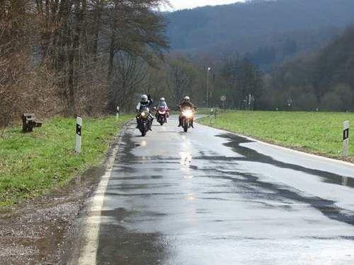 Drei Motorräder fahren auf einer nassen Landstraße in ländlicher Umgebung