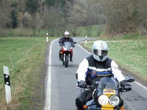 Zwei Motorradfahrer auf einer kurvigen Landstraße in einer ländlichen Umgebung