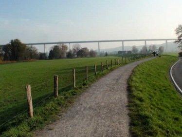 Landschaft mit Gehweg und Straßenverlauf neben einem grünen Feld unter einer Brücke