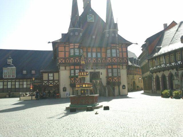 Fachwerkhaus mit spitzen Türmen und Uhr auf sonnigem Marktplatz mit Brunnen