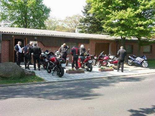 Mehrere Motorradfahrer mit ihren Motorrädern vor einer Reihenhausgarage unter Bäumen