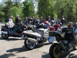 Mehrere Motorräder und eine Gruppe von Menschen im Freien auf einem Parkplatz bei sonnigem Wetter