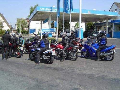Mehrere Motorradfahrer vor einer Tankstelle mit blauen Motorrädern und Helmen