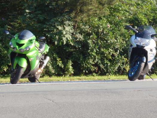 Zwei Motorräder, ein grünes und ein weißes, stehen am Straßenrand vor dichter Bepflanzung