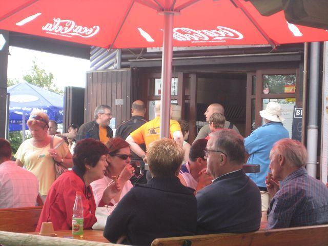 Menschen sitzen und stehen unter einem Coca-Cola-Sonnenschirm vor einem Gebäude