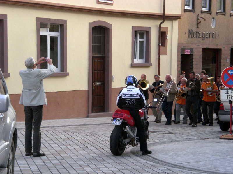 Person fotografiert Musikgruppe auf der Straße mit Motorrad im Vordergrund