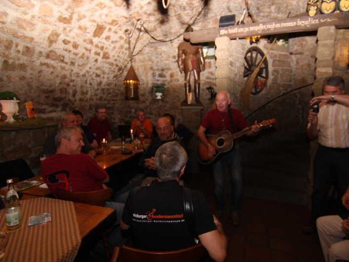 Gruppe von Menschen in einem Kellergewölbe, ein Mann spielt Gitarre und eine Person filmt