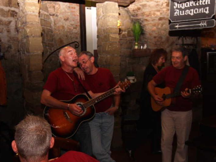 Drei Männer spielen Gitarre und singen in einem Raum mit Steinwänden