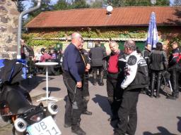 Gruppe von Menschen in Motorradkleidung unterhalten sich vor einem Gebäude mit rotem Ziegeldach