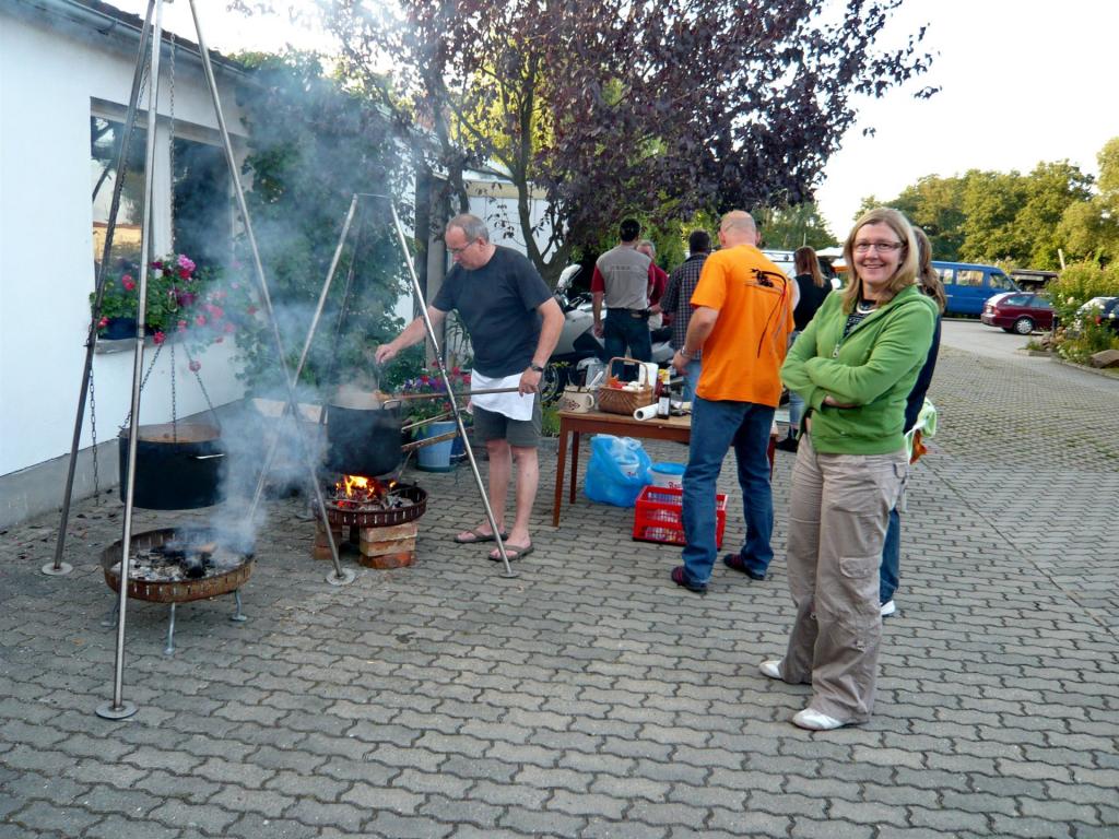 Menschen bei einer Grillveranstaltung im Freien neben einem weißen Gebäude mit rauchenden Grills