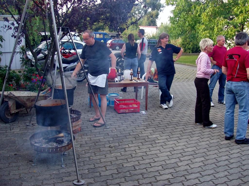 Mehrere Menschen beim Grillen und Unterhalten im Freien auf gepflastertem Hof