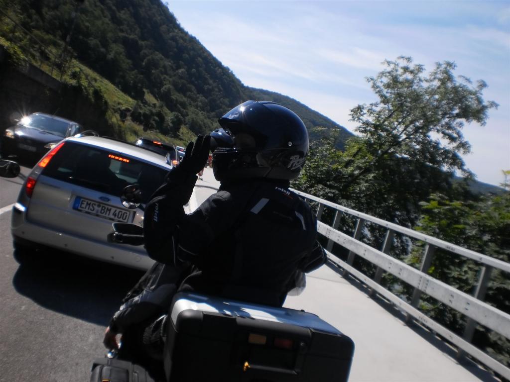 Motorradfahrer in schwarzer Schutzkleidung und Helm fährt auf einer kurvigen Straße mit Stau von Autos