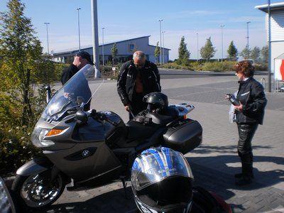 Drei Personen in Motorradkleidung stehen neben zwei Motorrädern auf einem Parkplatz.