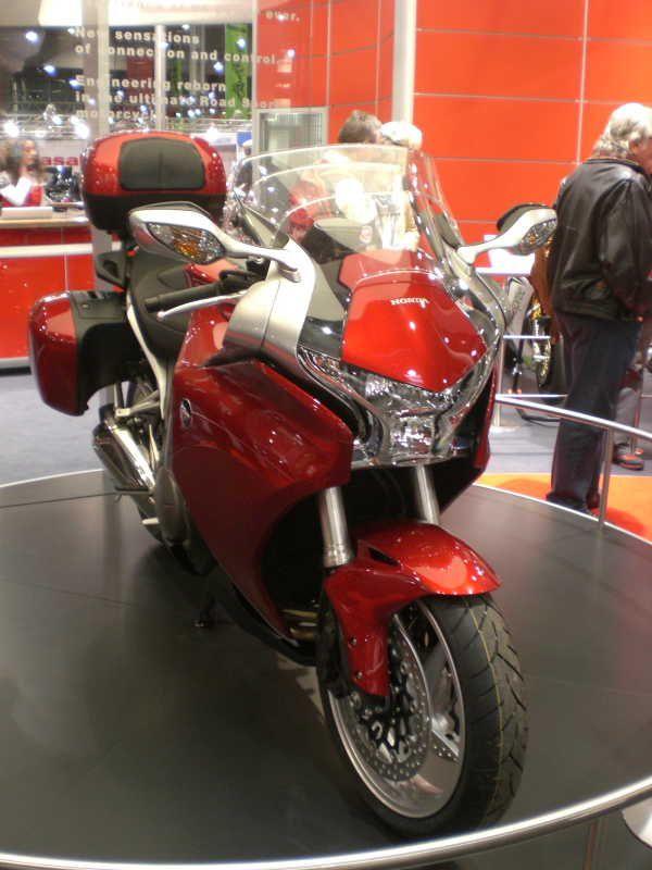 Rotes Honda Touring-Motorrad auf einer Ausstellungsplattform mit Personen im Hintergrund