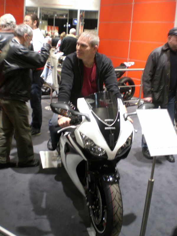 Mann sitzt auf einer weißen Honda-Sportmotorrad im Ausstellungsraum mit mehreren Personen im Hintergrund