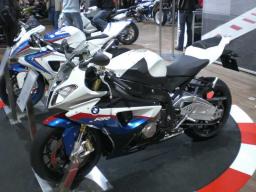 Sportliches BMW Motorrad in Weiß, Blau und Rot auf einer Messe mit weiteren Motorrädern im Hintergrund