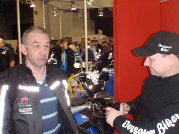 Zwei Männer in Motorradkleidung vor Motorrädern auf einer Messe