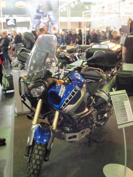 Blaues Gelände- oder Reise-Motorrad mit großem Windschutz und Gepäckkoffer auf einer Messe