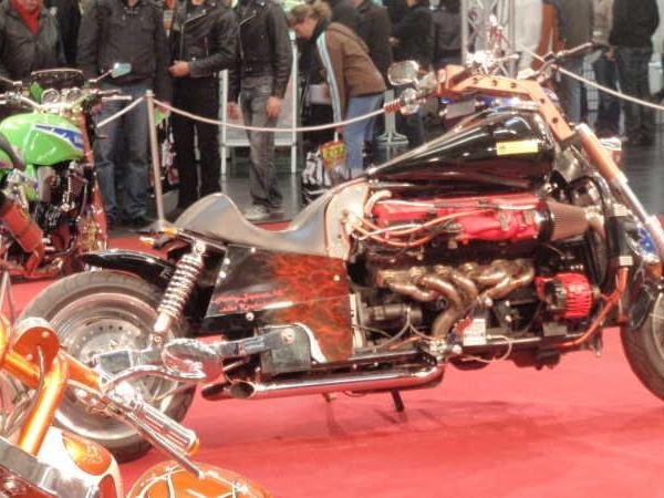 Eine individuell gestaltete schwarze und rote Maschine mit breitem Hinterrad auf einer Messe mit Besuchern im Hintergrund