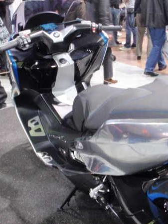Schwarzer Motorroller mit blauen Akzenten auf einer Messe mit Menschen im Hintergrund