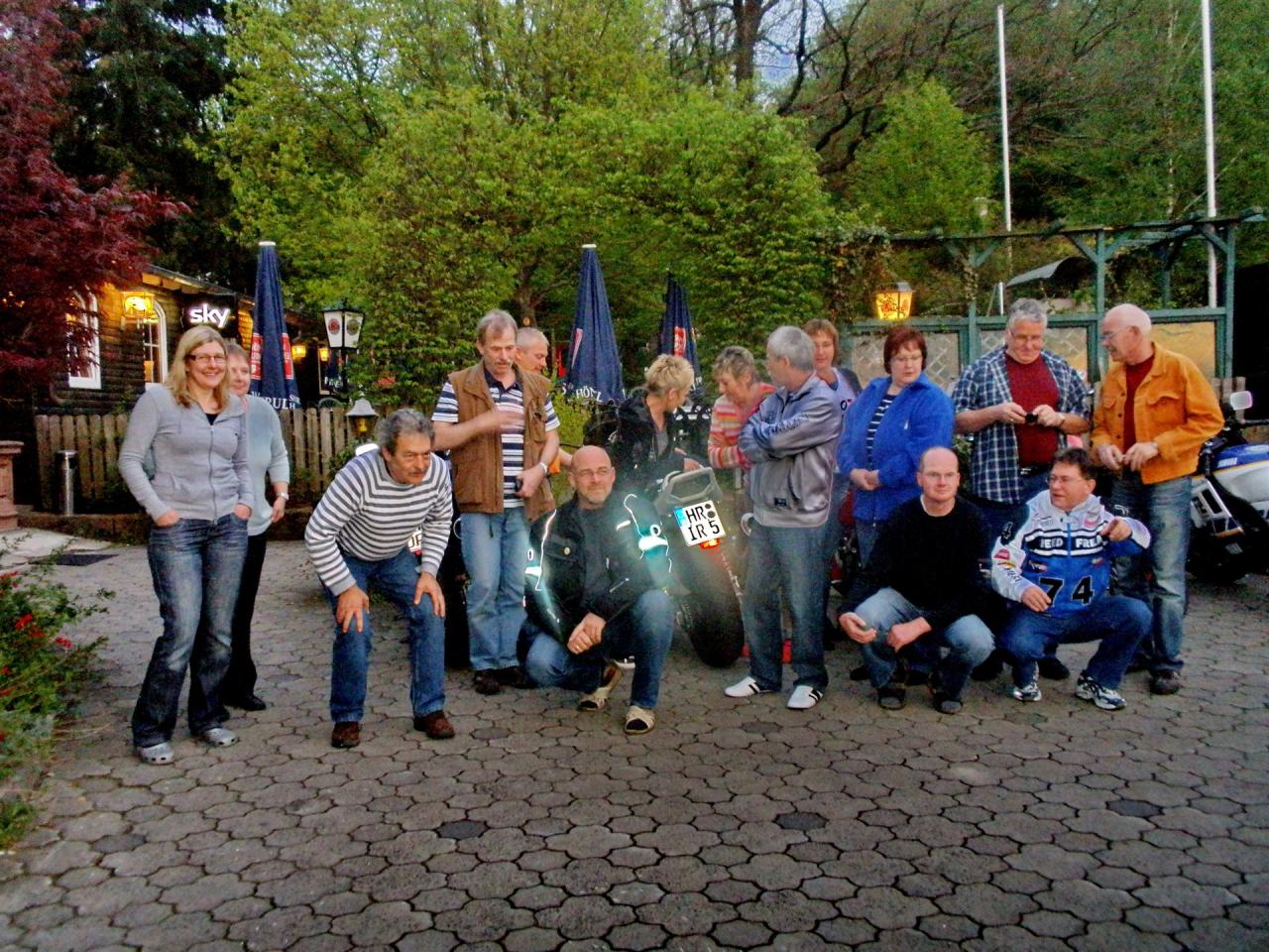 Gruppe von Menschen in lockerer Haltung im Freien vor Bäumen und Zelten