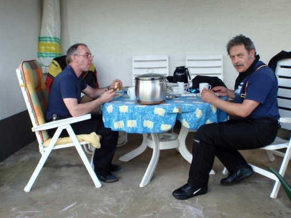 Zwei Männer sitzen an einem Tisch im Freien und essen zusammen.