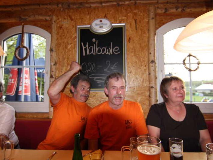 Menschen sitzen an einem Holztisch in einer gemütlichen Gaststube mit Fenstern und Getränken.