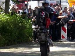 Motorradfahrer führt auf öffentlicher Straße einen Wheelie vor vor Zuschauern