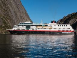 Passagierschiff Hurtigruten fährt durch norwegischen Fjord mit steilen Felswänden